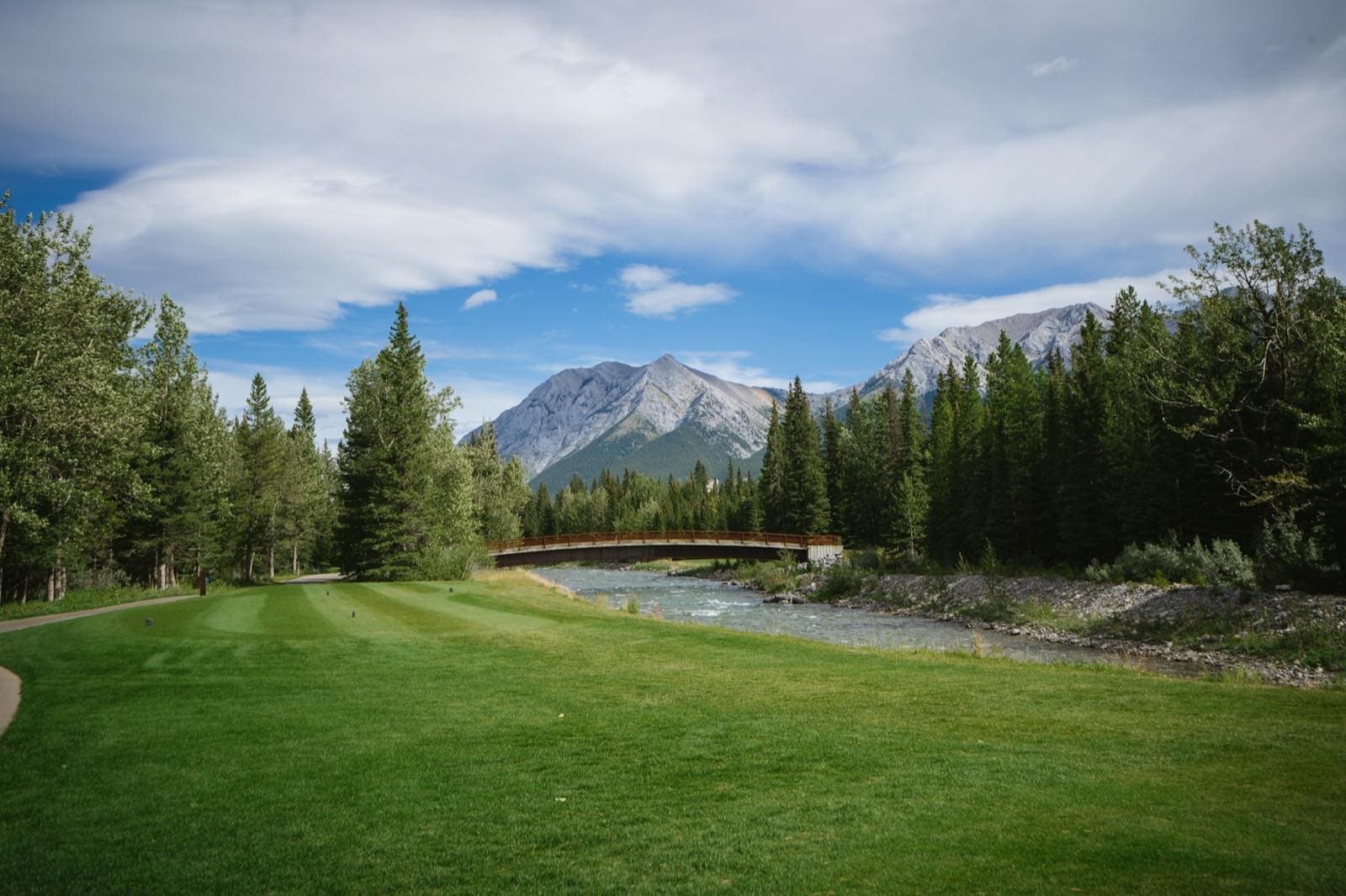 A real golf course beside a river, bridge, and mountain range